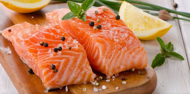 Two salmon fillets with cracked black pepper and salt on them.